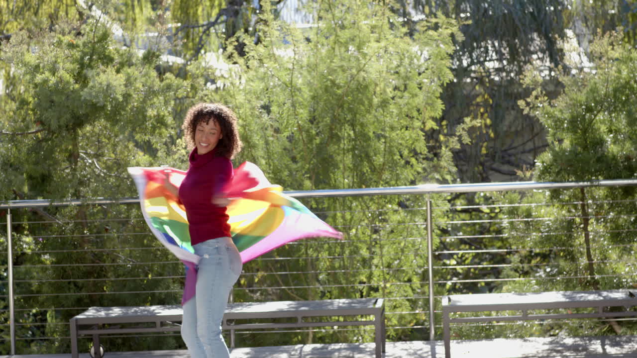 Smiling woman outdoors, waving rainbow flag and enjoying sunny day