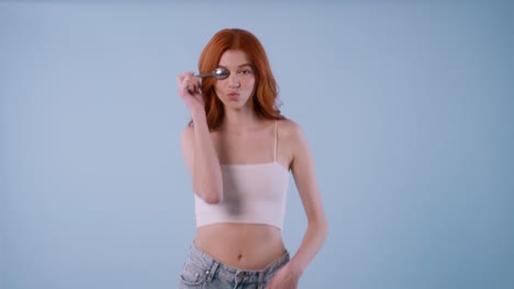 a young redhead model in crop top strikes various creative poses holding a spoon, using it like a prop in front of her eyes with a confident expression.