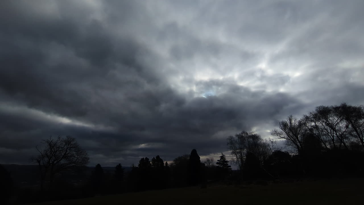 Ultra Wide View of Dark Stormy Clouds Over Silhouetted Trees with Big Lightning Thunder Strikes Behind Cloudscape with Sunlight Behind. Scary Spooky Storm VFX.