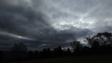 ultra wide view of dark stormy clouds over silhouetted trees with big lightning thunder strikes behind cloudscape with sunlight behind. scary spooky storm vfx.