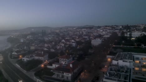 Aerial,-tracking,-drone-shot-panning-around-the-coast-of-Cascais-cityscape,-during-night-time,-in-Lisbon,-Portugal