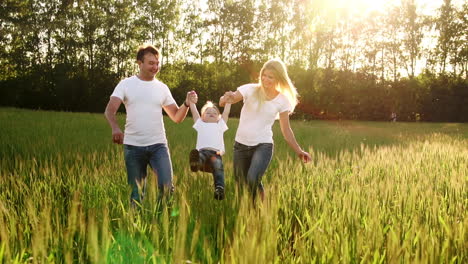 mother father and son walk in the field with spikes in white t-shirts and jeans fun swinging it on his hands