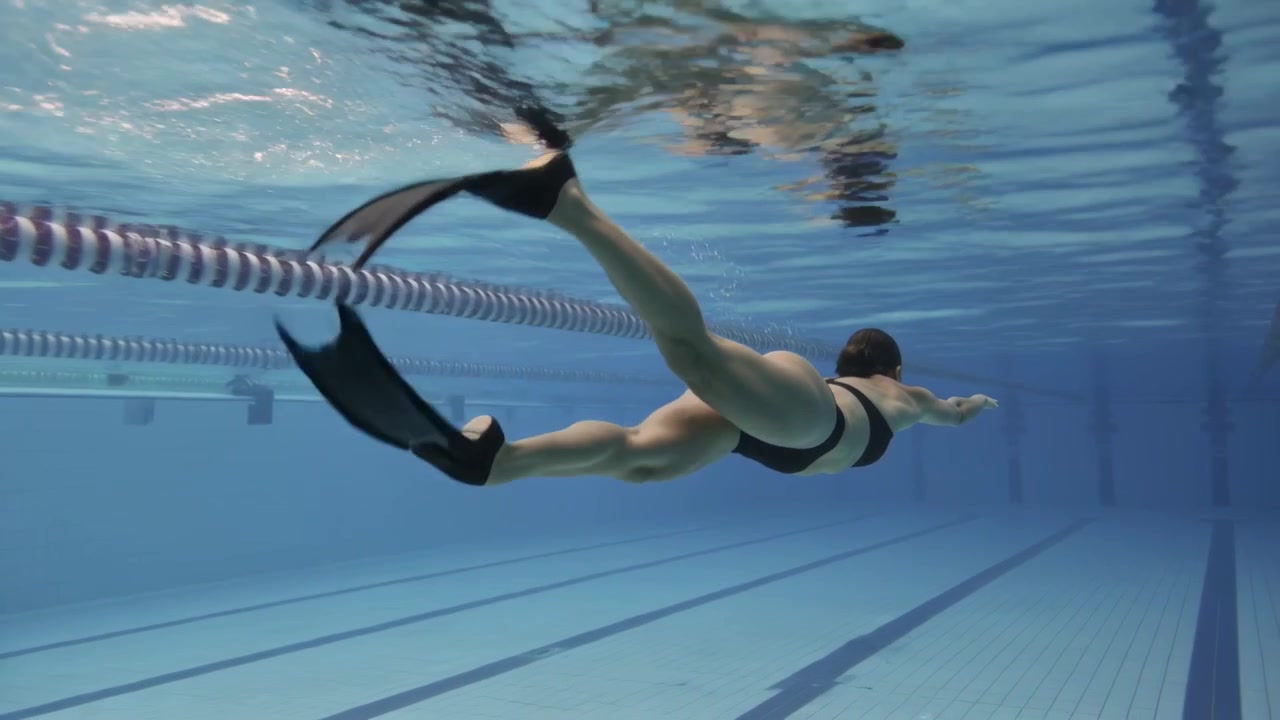 Initiating fin kicks from streamline, swimmer practicing laps in dark suit, cap passing lane rope