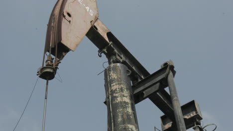 an oil pumpjack rises and falls as clouds pass across a blue sky in time lapse