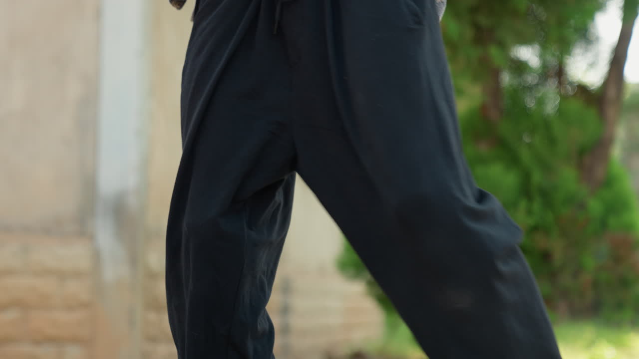Siyahi erkek spor ayakkabısı yakın çekim, dışarıda tekme atıyor, dar siyah pantolon, dinamik ayak hareketi, güçlü taban darbesi, beton dokusu, antrenman enerjisi, atletik odak, tekrarlayan pratik, sokak sporu.