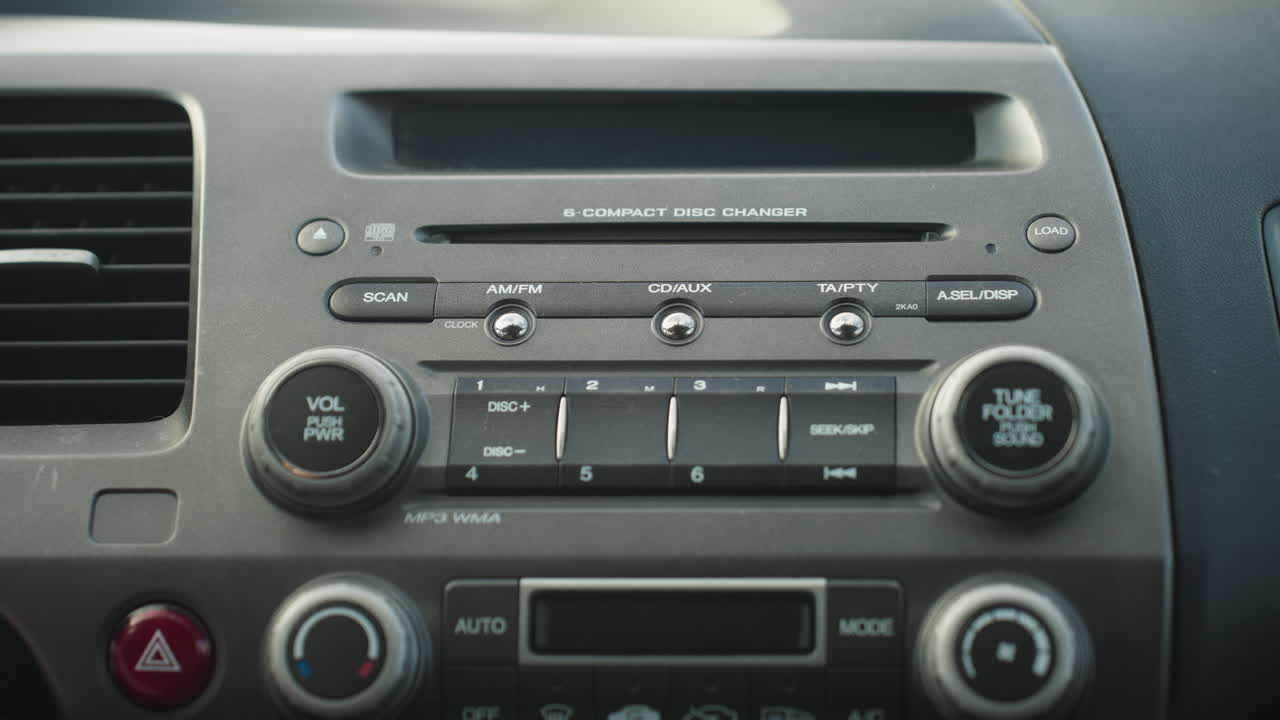 close up of car stereo system showing hand adjusting volume knob as vehicle is powered on, dashboard layout includes control buttons and CD changer with detailed focus on textures and labels