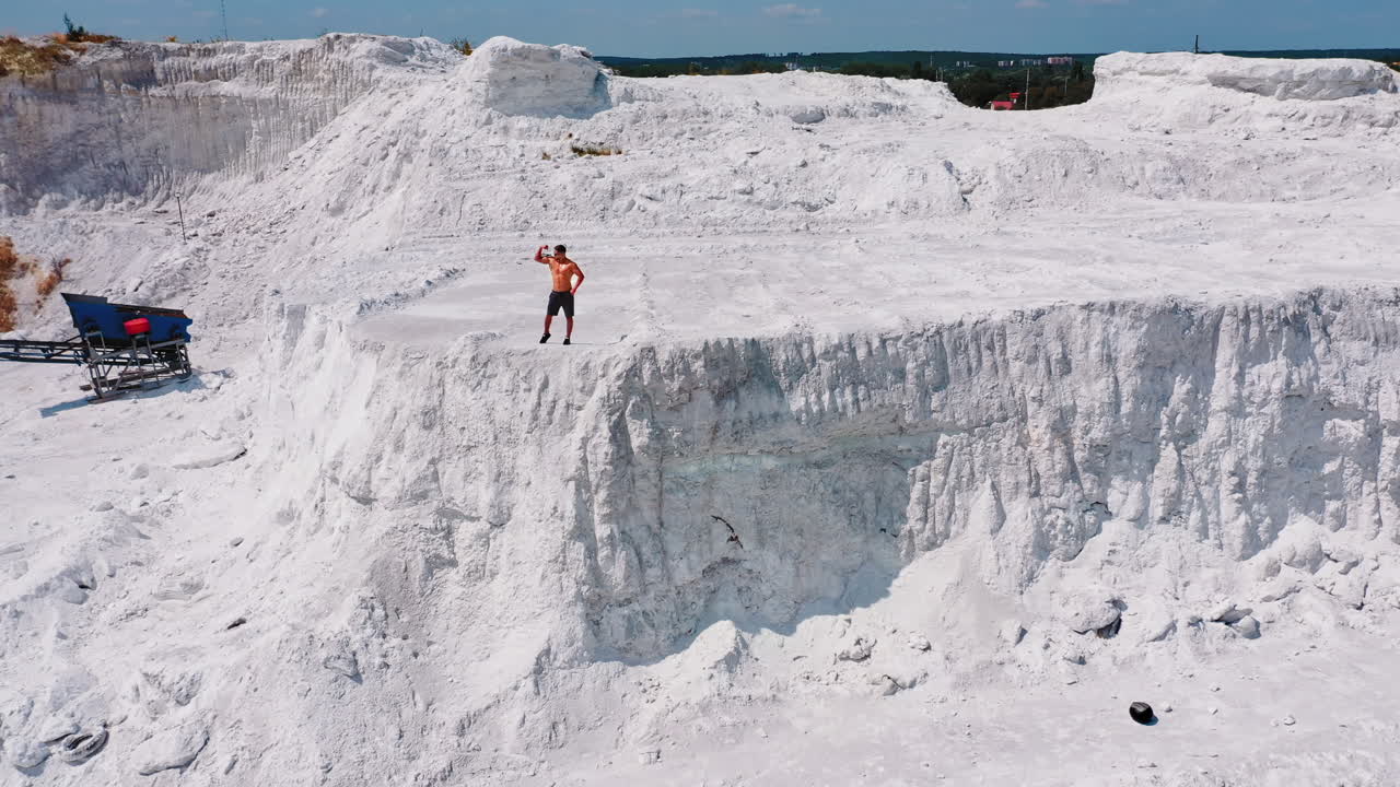 Muscular sportsman on a white hill. View from above on a strong guy who is showing his strength on the natural background. Bodybuilder on a rocky canyon. Aerial view.