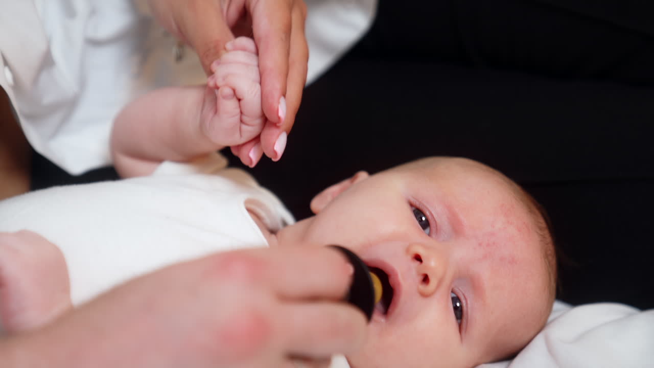 Little Caucasian newborn is going to cry. Baby lies on its back and tries to scream but mom gives him a pacifier. Close up.