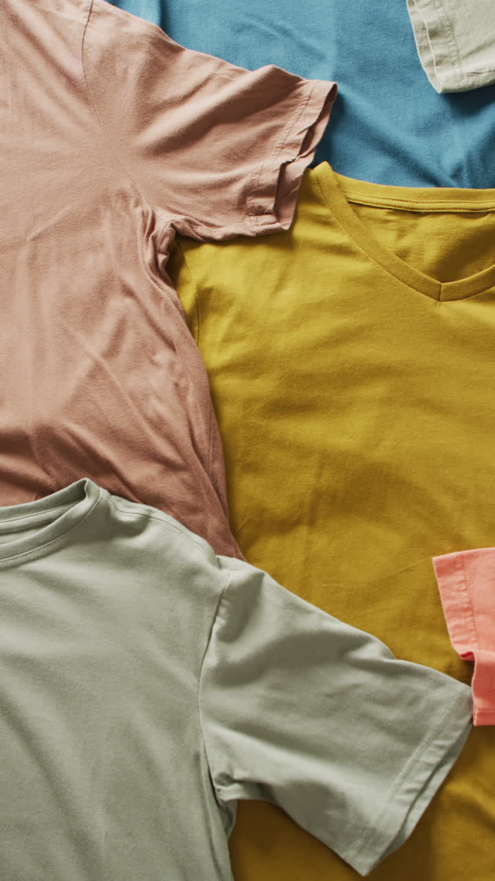 Vertical video of close up of layers of multiple t shirts background with copy space