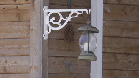 detail of a retro metal lantern with a candle inside, hanging from a wooden house and swinging in the wind