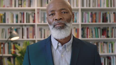 portrait of senior african american businessman with beard looking serious at camera removes glasses successful black male executive in library study background