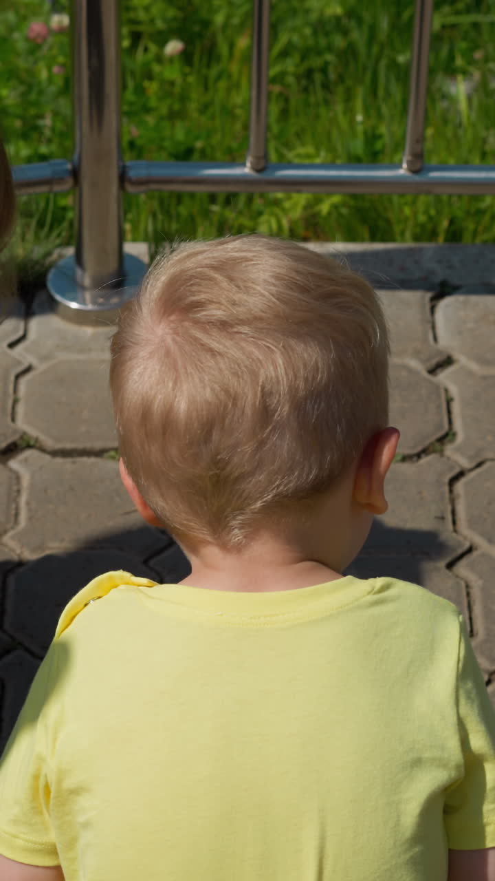 사랑스러운 작은 형제 자매는 은 날 푸른 공원에서 금속 울타리 근처의 포장 도로에서 달리는 개미를 보십시오.