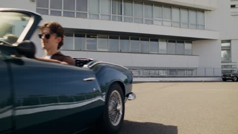 couple in vintage convertible car in front of modern building