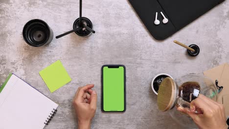 work desk with smartphone and office supplies, top view. female hands pouring black coffee into white cup at work table. woman pouring steaming coffee into cup on work desk when work from home