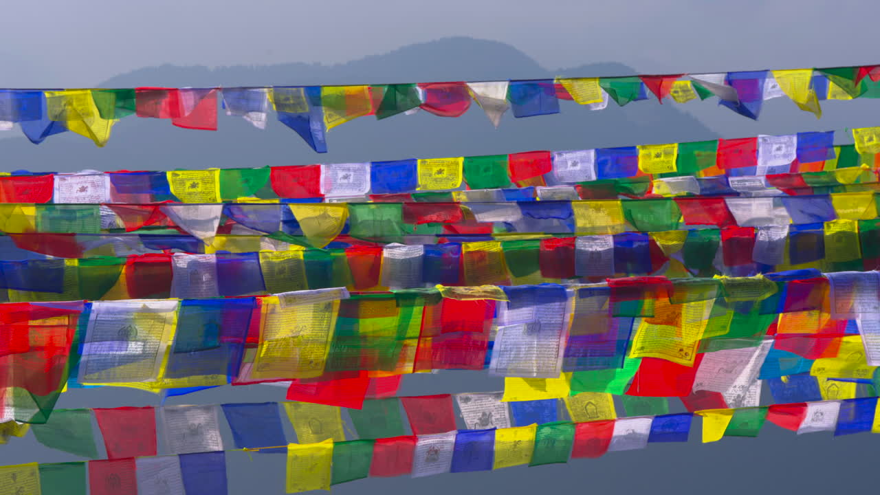 Rows of colorful prayer flags with sacred symbols stretching across the frame with a misty blue mountain ridge under a pale sky at Ama Yangri Nepal
