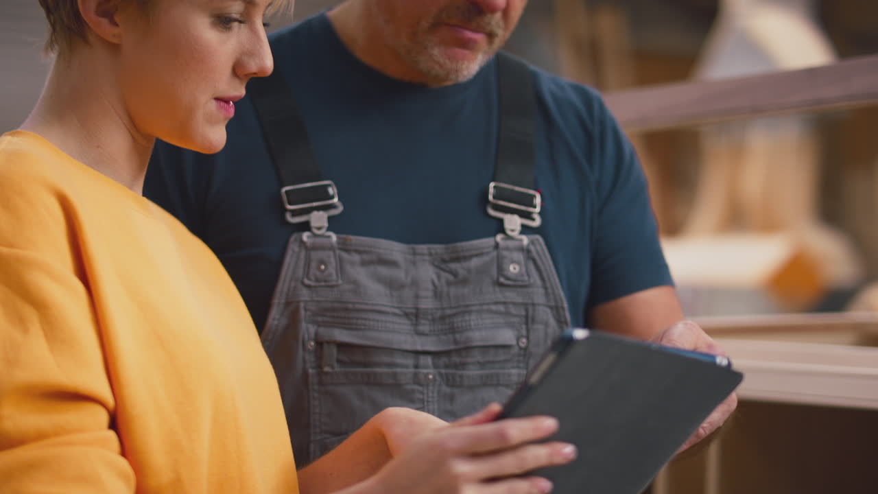 aprendiz femenina aprendiendo de un carpintero adulto con una tableta digital en un taller de muebles