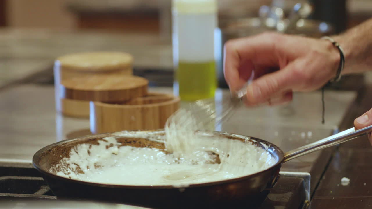 프라이팬에 화이트 소스를 휘젓는 남자의 손, 느린 동작
