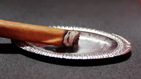 cigarro encendido descansando sobre cenicero de plata