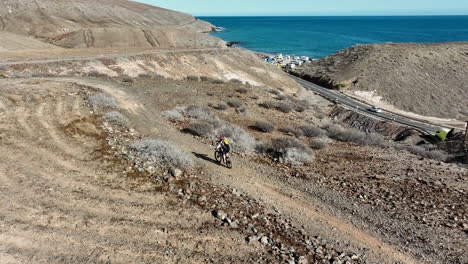 fantastic lateral aerial shot of a man with his mountain bike in a desert landscape and where you can see the coast and the sea