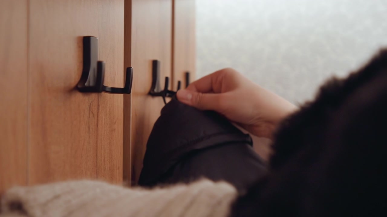 Momento accogliente con mano attenta. Scena delicata di una mano che sistema una giacca vicino a un ambiente con coperta calda. Ambiente domestico calmo che mostra una mano che sistema un cappotto su un appendino di legno con dintorni accoglienti