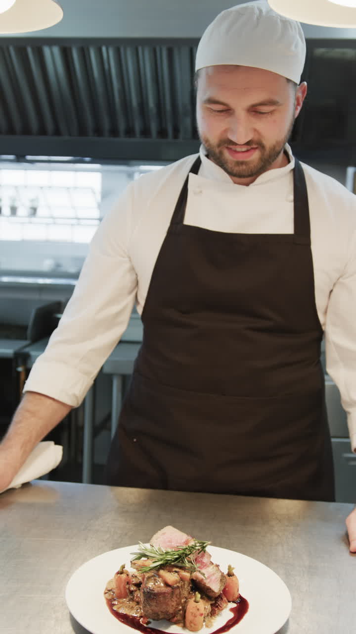 Happy caucasian male chef with finished decorated meal on plate in kitchen, slow motion, vertical