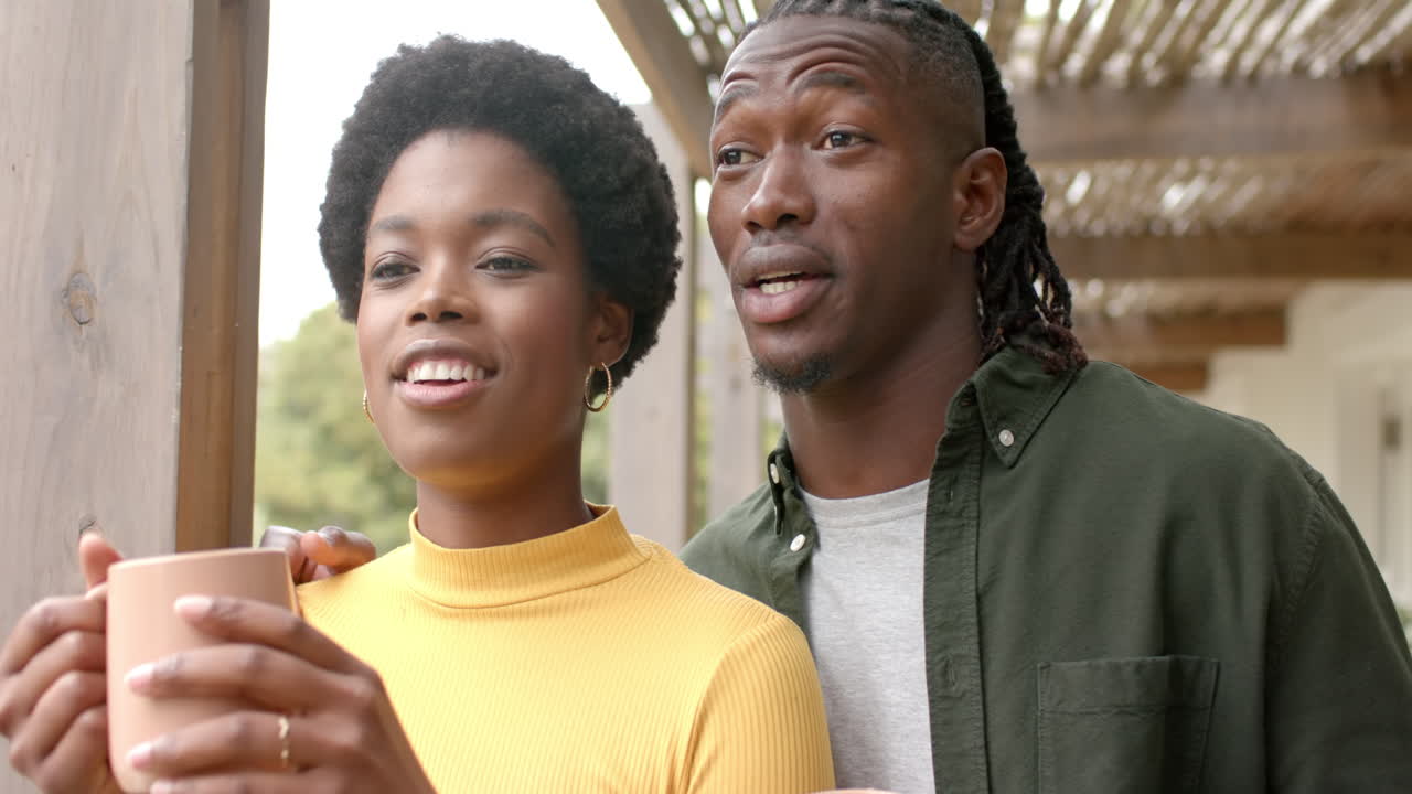 Smilende afroamerikansk par nyder kaffe sammen, slapper af derhjemme på en solrig dag