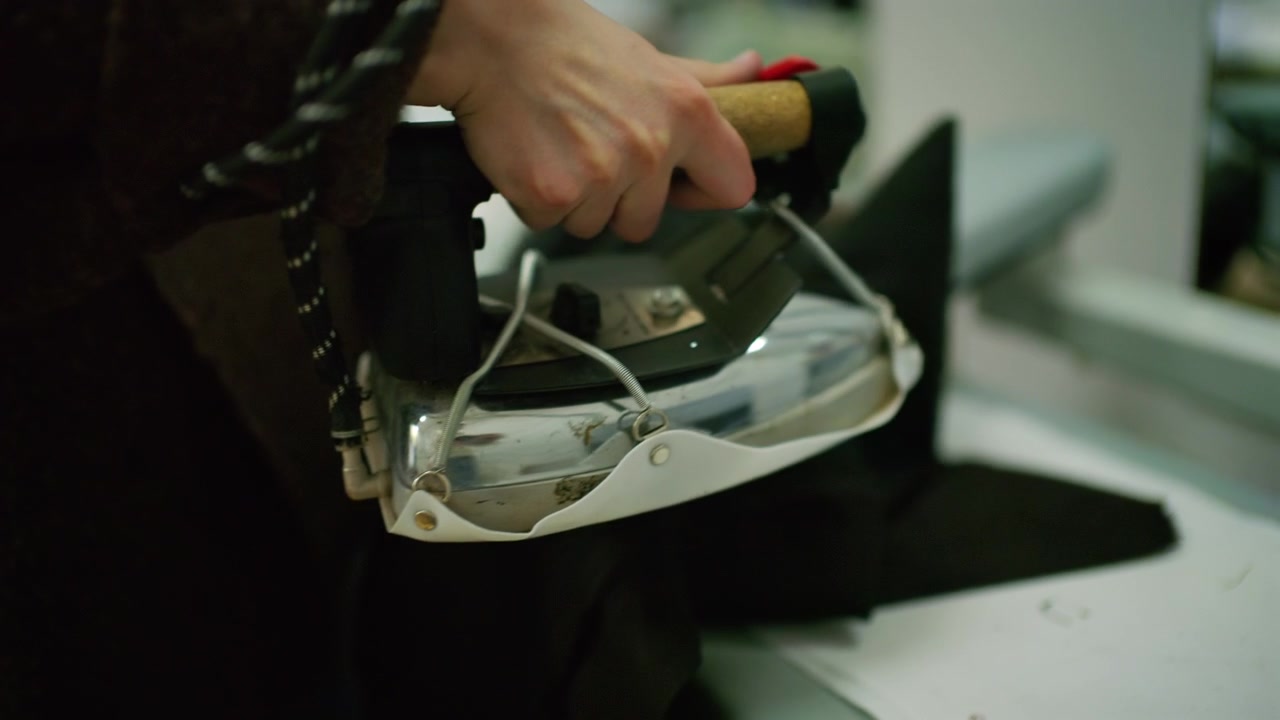 Close up of a tailor using a professional steam iron on black fabric in a fashion workshop