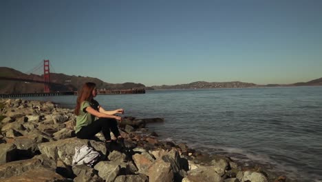 Woman-sitting-on-rocks-beside-the-Golden-Gate-Bridge