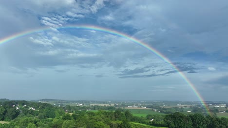 magnificent rainbow at sky over green hills and farm fields of america. rural area in countryside of usa. aerial panning wide shot. quiet atmosphere outdoors