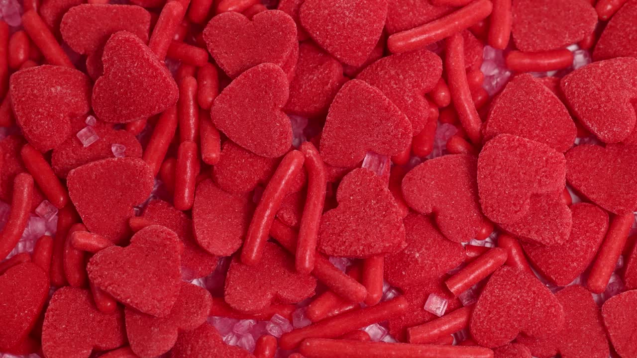 Close-up of red heart-shaped candies and sprinkles rotating, creating a vibrant, textured pattern in bright lighting
