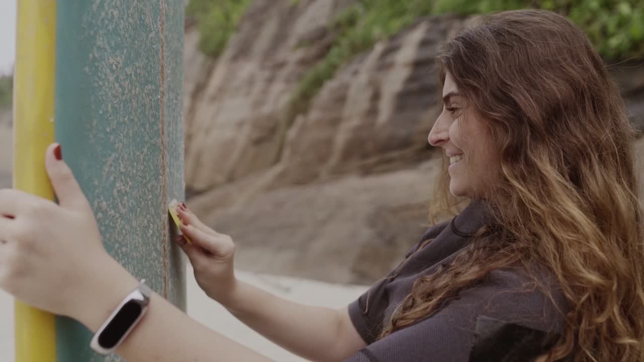 Woman waxing a surfboard on the beach, smiling