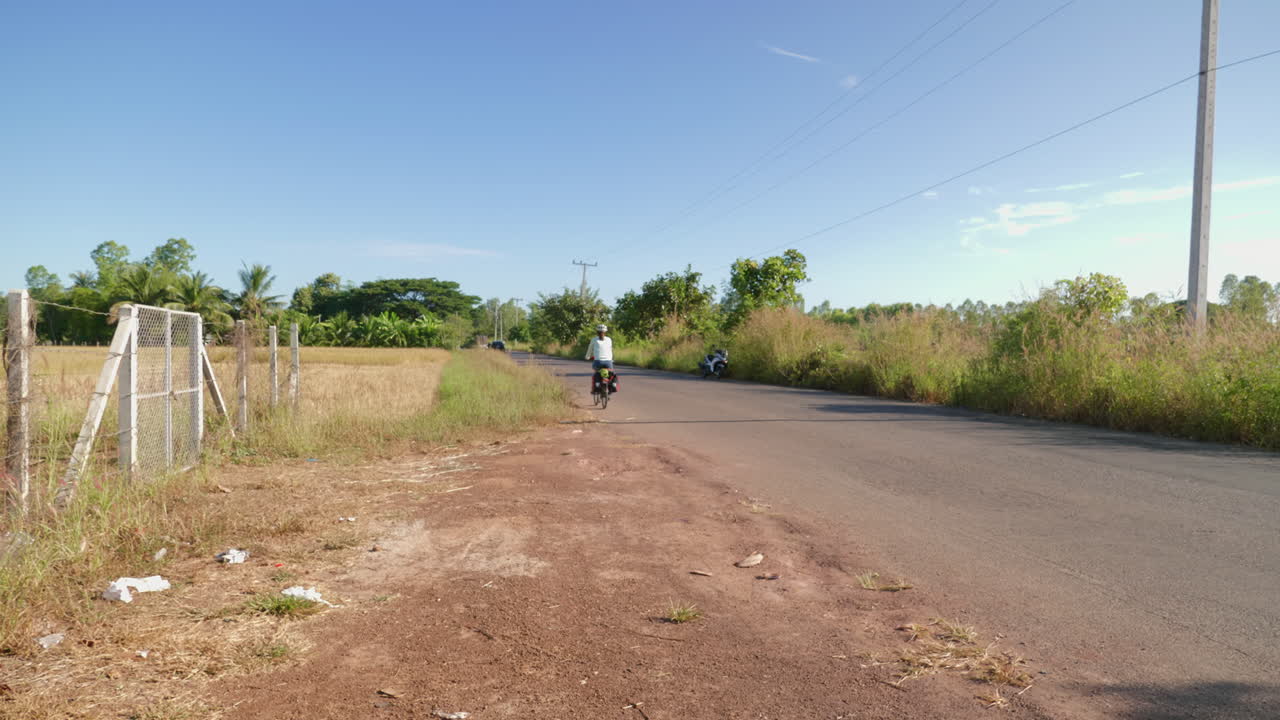 A solo Asian woman long distance cyclist and backpacker dressed in athletic clothes riding through the road of Udon Thani on her foldable bicycle on the left corner of the road, Thailand