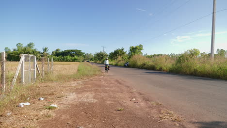 Una-Ciclista-Asiática-Solitaria-De-Larga-Distancia-Y-Mochilera-Vestida-Con-Ropa-Atlética-Recorriendo-La-Carretera-De-Udon-Thani-En-Su-Bicicleta-Plegable-En-La-Esquina-Izquierda-De-La-Carretera,-Tailandia