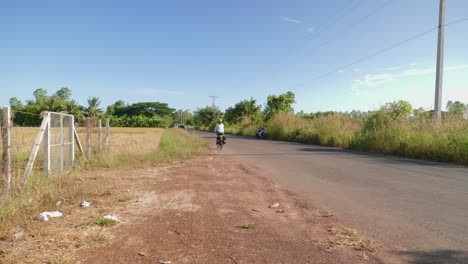 una ciclista asiática solitaria de larga distancia y mochilera vestida con ropa atlética recorriendo la carretera de udon thani en su bicicleta plegable en la esquina izquierda de la carretera, tailandia