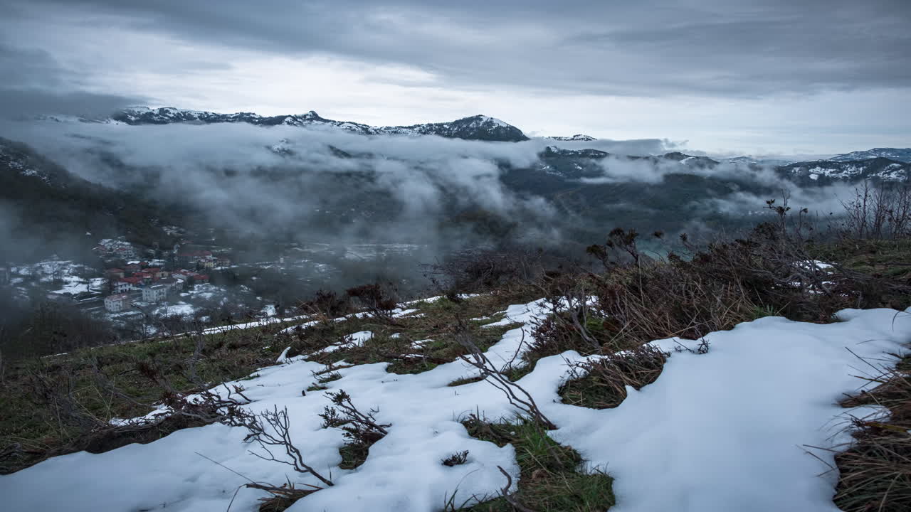 Misty mountains with snow foreground and a glimpse of a valley, shot during dusk, timelapse