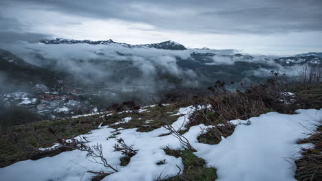 Misty-mountains-with-snow-foreground-and-a-glimpse-of-a-valley,-shot-during-dusk,-timelapse