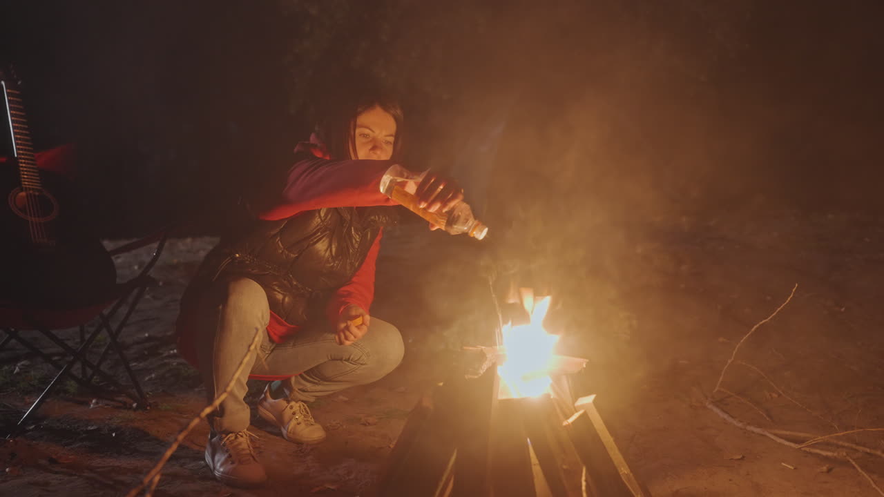 Mulher em acampamento controlando habilmente um clarão súbito e chamas crescentes de uma fogueira. Cena noturna ao ar livre com a mulher gerenciando cuidadosamente um fogo intenso que se espalha rapidamente.