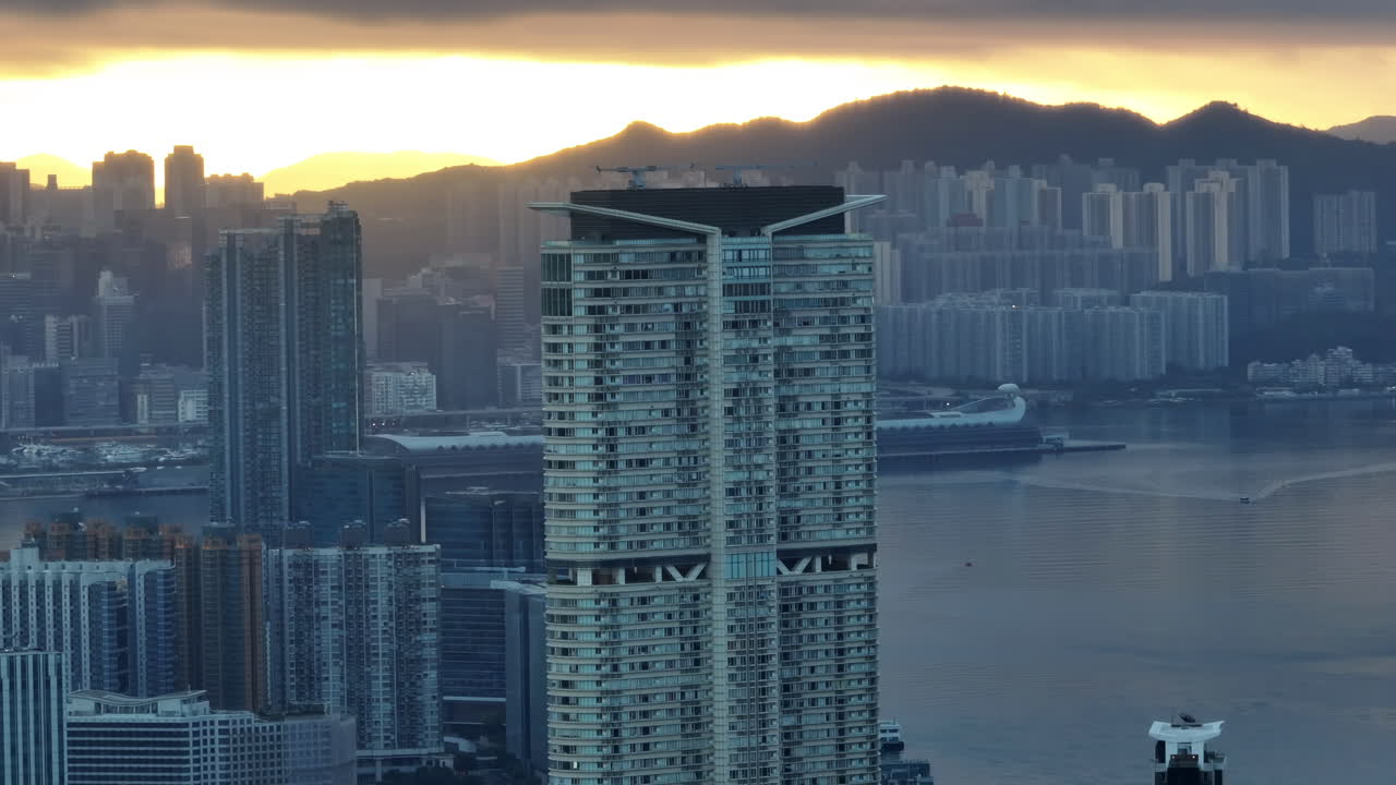 Tomada parallax de drone do arranha-céu K11 ao nascer do sol, com o Terminal de Cruzeiros Kai Tak ao fundo.
