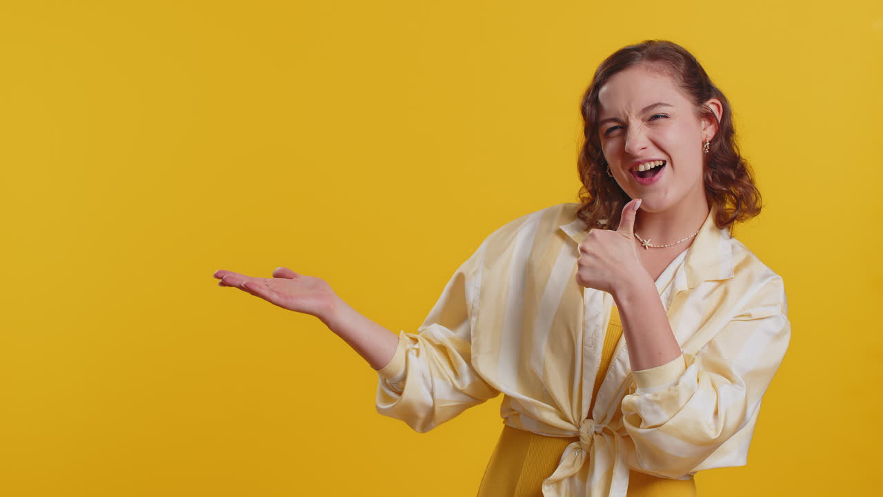 mujer joven mostrando los pulgares hacia arriba y señalando a la izquierda en el espacio en blanco lugar para su logotipo de publicidad