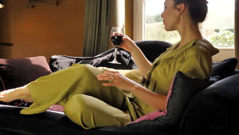 classy white caucasian woman sitting down in couch, relaxing, holding a glass of wine, slow motion