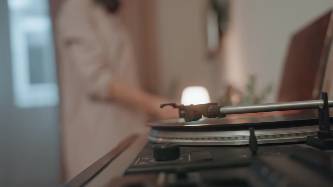 Signora allegra che balla tra le luci accoglienti di casa. La donna si muove felicemente accanto al giradischi in un'illuminazione calda, provando gioia con luci soffuse e gesti giocosi.