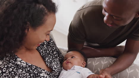 loving parents sitting in chair cuddling baby son in nursery at home