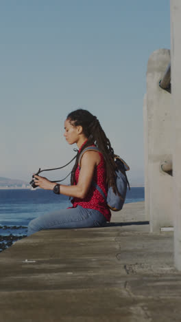 Animación-De-Puntos-De-Luz-Sobre-Una-Mujer-Birracial-Sentada-Con-Binoculares-En-El-Paseo-Marítimo