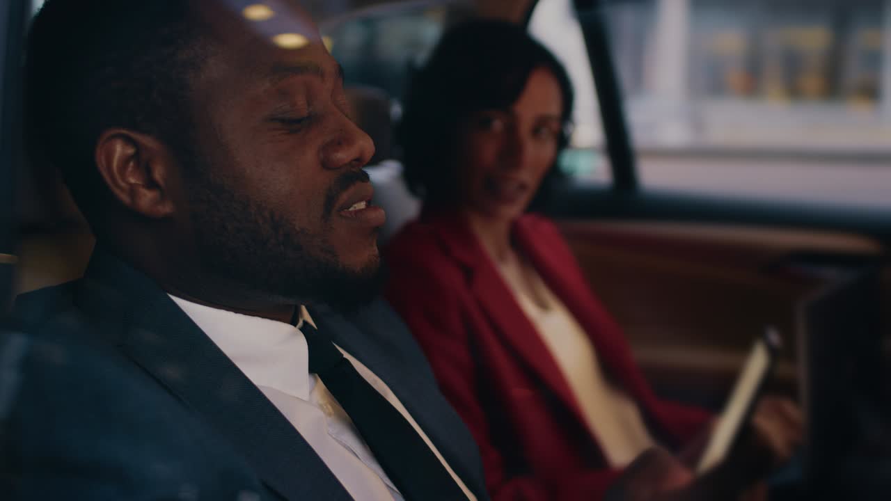 한 사업가와 사업가가 저녁에 차 뒷좌석에 앉아있고, 한 남자가 스마트폰을 사용하고, 아내와 대화를 나누고, 카메라 이 차 밖에서 찍혔습니다.