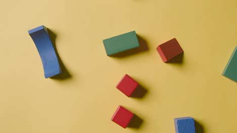 overhead shot of colourful wooden building blocks being thrown onto yellow studio background