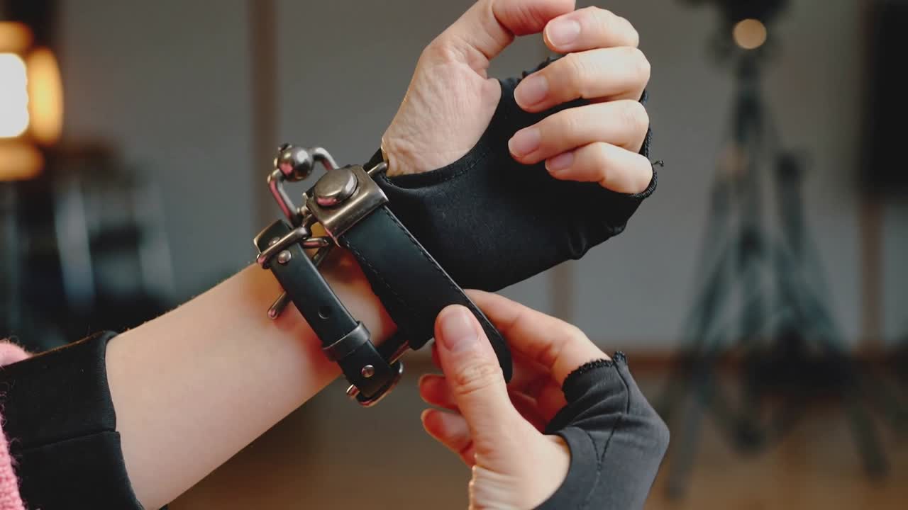 Eine behandschuhte Hand reagiert auf eine lockere Manschette, fädelt einen Riemen ein und strafft die Manschette am Handgelenk eines pinkfarbenen Ärmels im Studio.