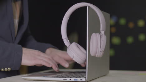 Salesperson-typing-fast-on-laptop-with-headphones-on-monitor,-close-up