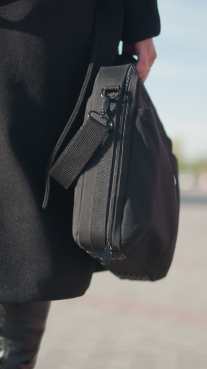 멋진 검은 코트와 부츠를 입고 두 개의 가방을 들고, 한 손으로 빛으로 빛나는 도시 거리에서 코트를 조정하고, 주차된 자전거의 흐릿한 시야에서 자신감 있게 는 여성의 클로즈업