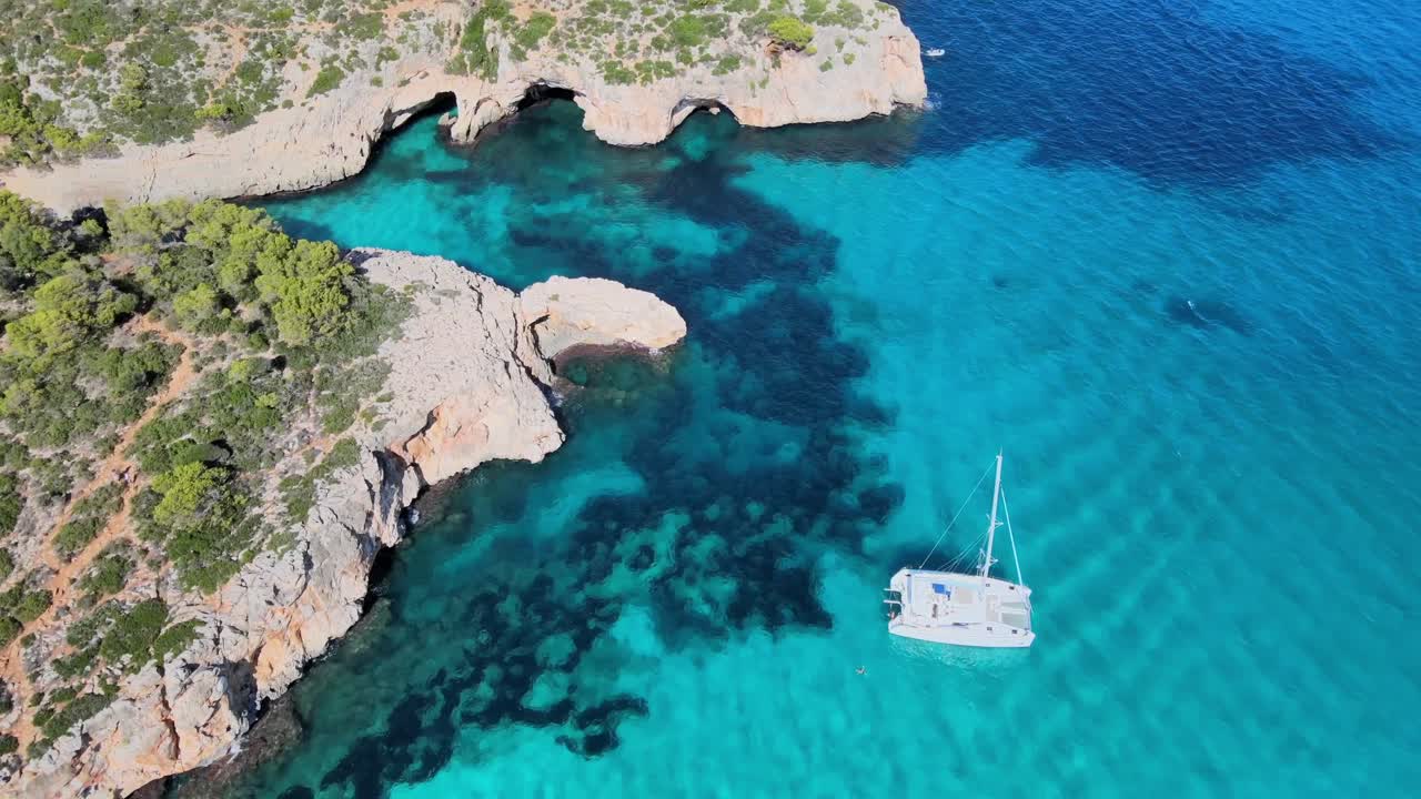 Experience the crystal-clear waters and rugged coastline of Cala Varques near Porto Cristo. Sailboats glide through beautiful bays surrounded by natural beauty and tranquility.