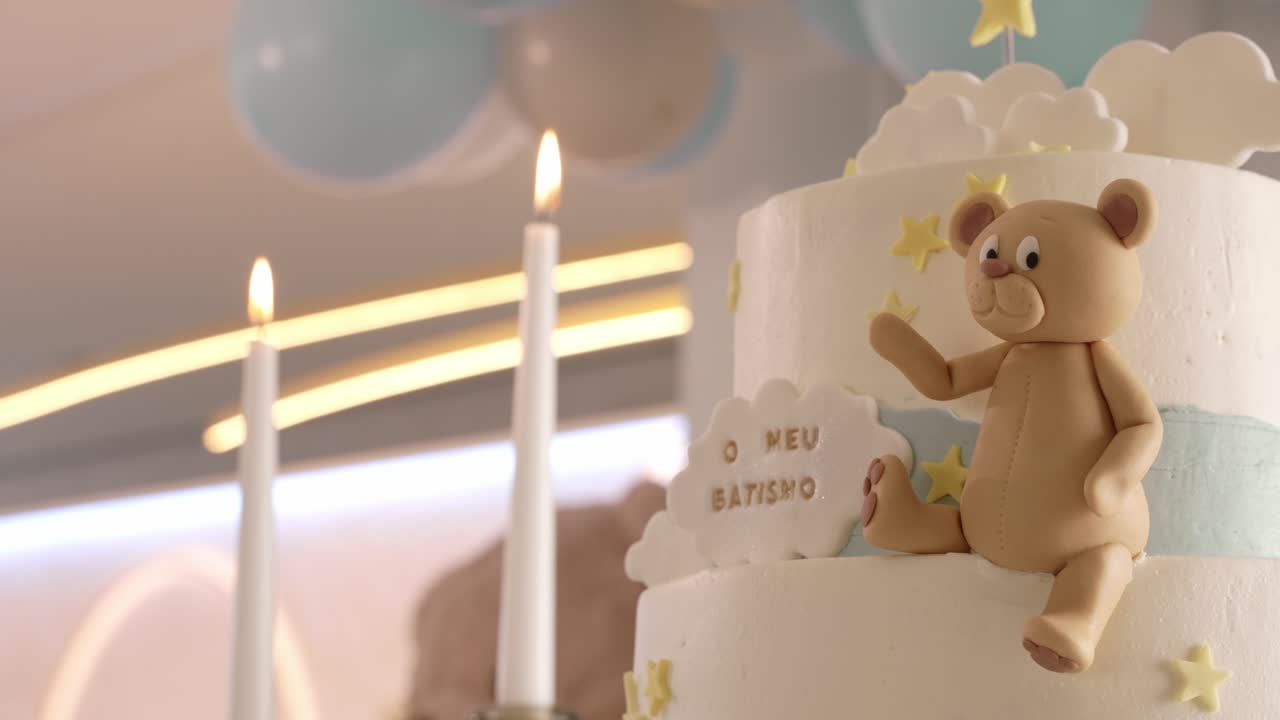 Pastel de bautizo de varios pisos con adorno de osito de fondant y velas encendidas a su lado